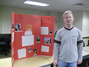 Me next to my project; I'm not wearing my glasses because they were still getting used to the lack of sunlight. How do you like my poster?